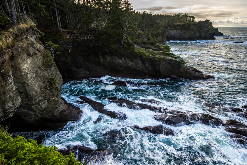 Cape Flattery coastal cliffs with turquoise water surging through rocky sea channels below forested headland
